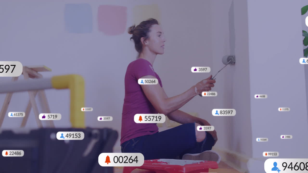 Animation of media icons over caucasian woman painting walls at home