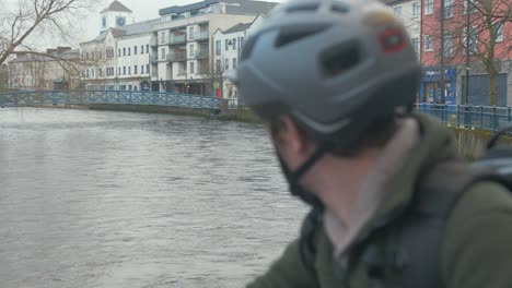 male cyclist looks out over flowing river by city