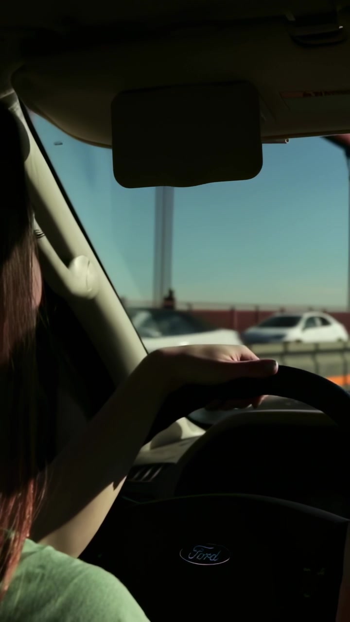 Video verticale: Donna alla guida con top verde che sterza, controlla lo specchietto superando auto su un ponte rosso, volante.