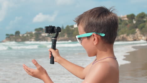 Joyful-vlogger-boy-talking-to-camera-at-seaside.-Cheerful-guy-filming-outdoor.