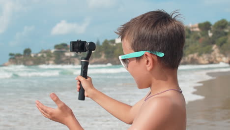 Alegre-Chico-Vlogger-Hablando-Con-La-Cámara-En-La-Playa.-Chico-Alegre-Filmando-Al-Aire-Libre.