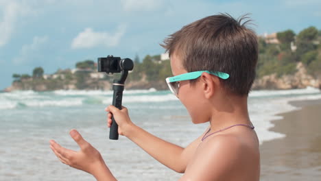 chico vlogger alegre hablando a la cámara en la playa. chico alegre filmando al aire libre.