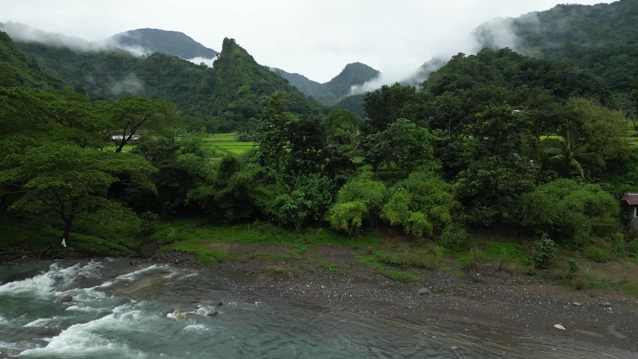 Wide aerial view of a Philippine valley with a winding river, red-roofed village, and mist-covered forested mountains blending natural beauty and rural life