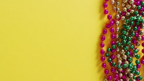 video of pink, gold and green mardi gras carnival beads on yellow background with copy space