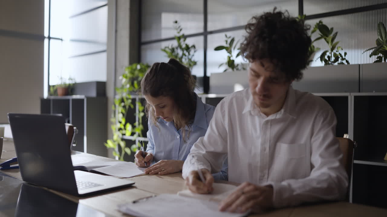 Two people working on a laptop and documents in an office setting