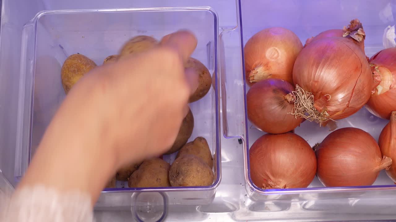 Mano che prende una patata dal cassetto del frigorifero, tra le cipolle