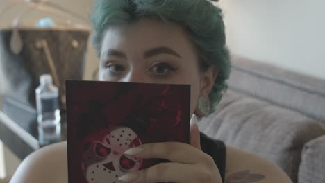 green-haired woman looking at the small mirror she holds in her hand to see if her makeup is good