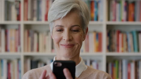 portrait beautiful senior business woman using smartphone enjoying browsing online texting reading funny messages smiling happy in bookshelf background