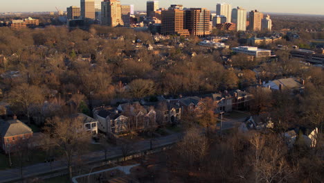 Flyover-houses-in-a-city-neighborhood-and-approaching-downtown-skyline-at-sunset