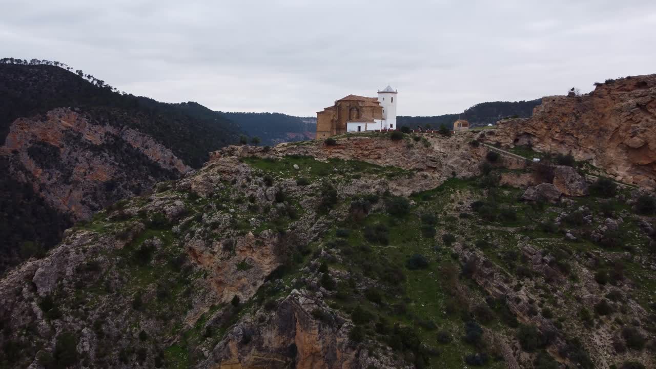 Ripresa aerea cinematografica in 4K di una chiesa spagnola bianca arroccata su una collina rocciosa. Vista panoramica del profondo canyon del fiume Júcar con acque turchesi e scogliere calcaree in Castilla-La Mancha, Spagna