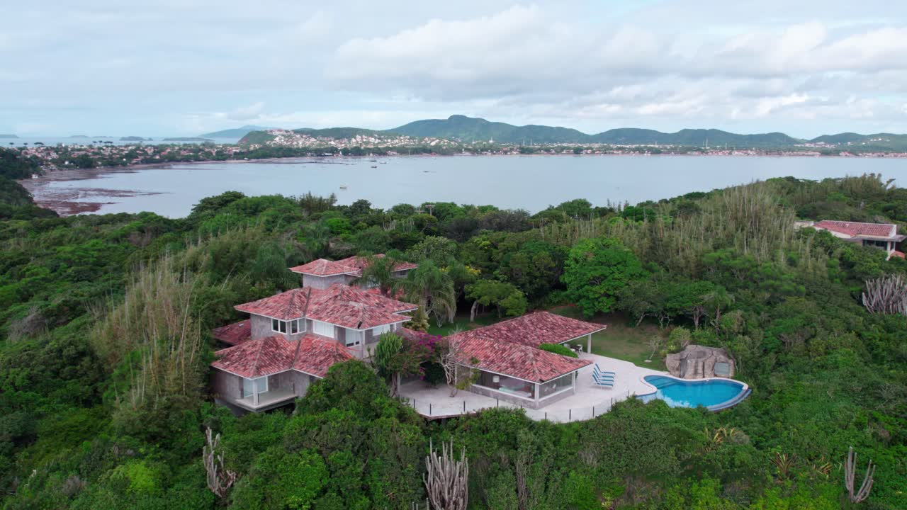 Aerial orbit of a mansion with swimming pool without people in B&uacute;zios, Brazil among a lush jungle and tropical climate