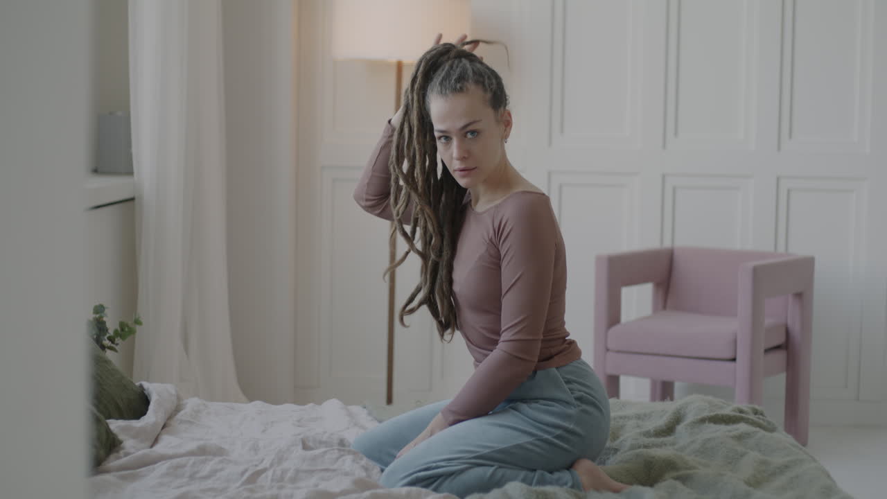 Woman with dreadlocks sitting on a bed in a bedroom