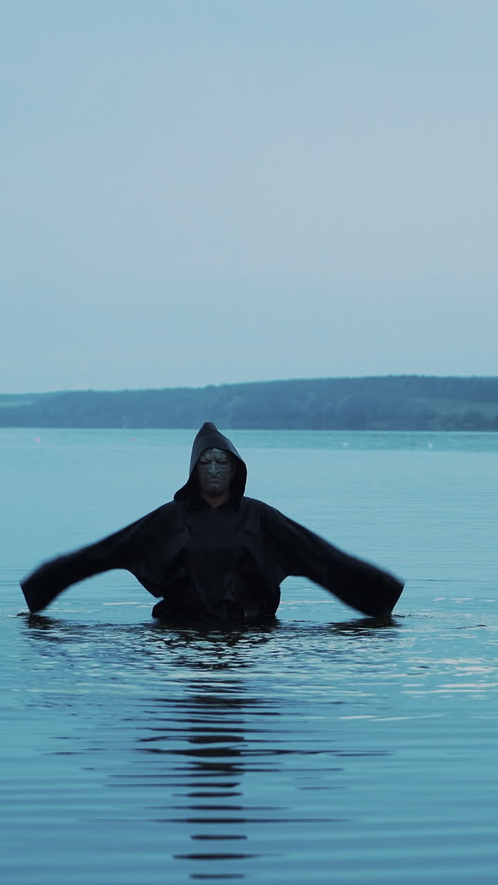 Terrible figure in a black robe in the water outdoor. Divination by Halloween Vertical video