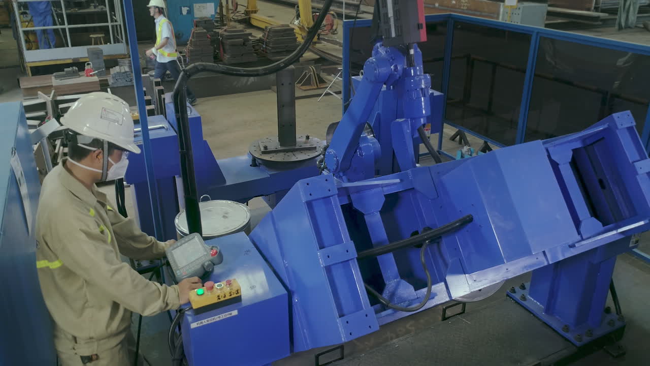 Man In Hard Hat And Mask Monitoring A Robotic Welding Machine. high angle