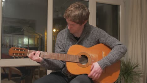 hombre aprendiendo guitarra acústica en casa plano medio