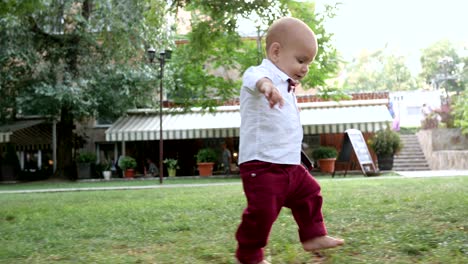 slow motion video footage of first steps of kid, attractive little child walking by himself barefoot on green grass