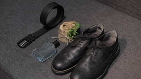 wedding details of groom. bridegrooms perfume, belt, shoes and wedding rings lie on sofa