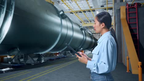 vista lateral de una mujer de negocios asiática usando una tableta mirando a su alrededor en una fábrica de fabricación de tubos