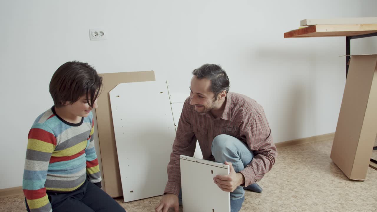 padre e hijo se comunican alegremente y montan muebles de acuerdo con las instrucciones en el suelo de la habitación. ayudar con la tarea. ahorrar el presupuesto familiar. compra a través de internet