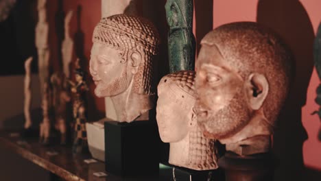 Close-up-of-multiple-ancient-antique-male-statues-heads-in-a-museum-with-moody-warm-lights