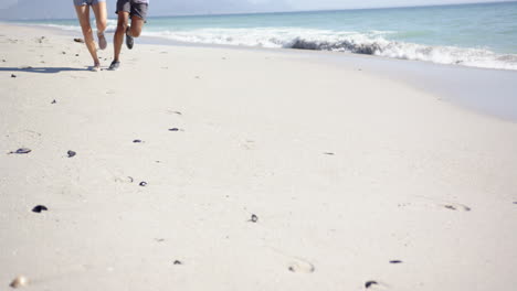 dos personas están corriendo a lo largo de una playa de arena, dejando huellas en su seguimiento, con espacio de copia