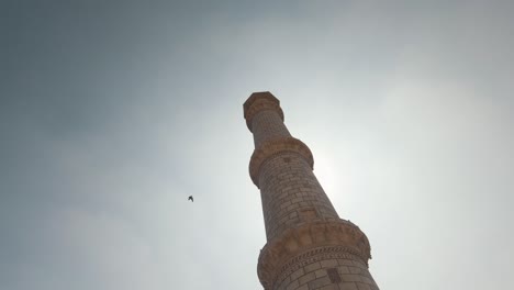 midday sun shining through tall minaret standing beside taj mahal  - wide low angle slow panning shot