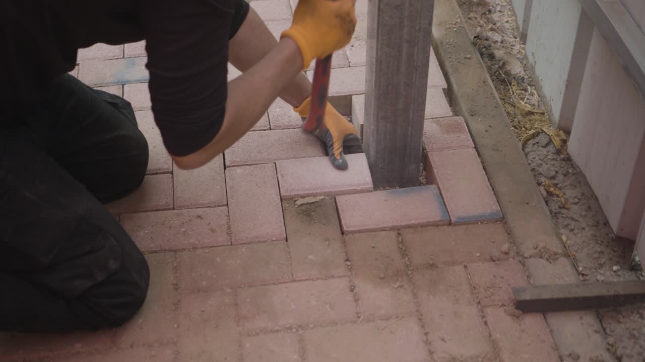Worker places paving stone with rubber mallet around a concrete post during outdoor construction landscaping project