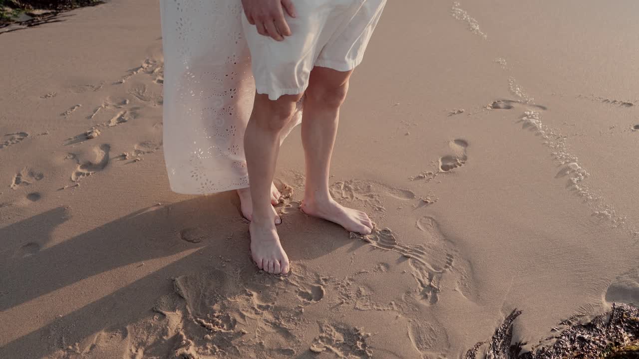 close up of man and woman standing barefoot on the beach with soft sand and footprints