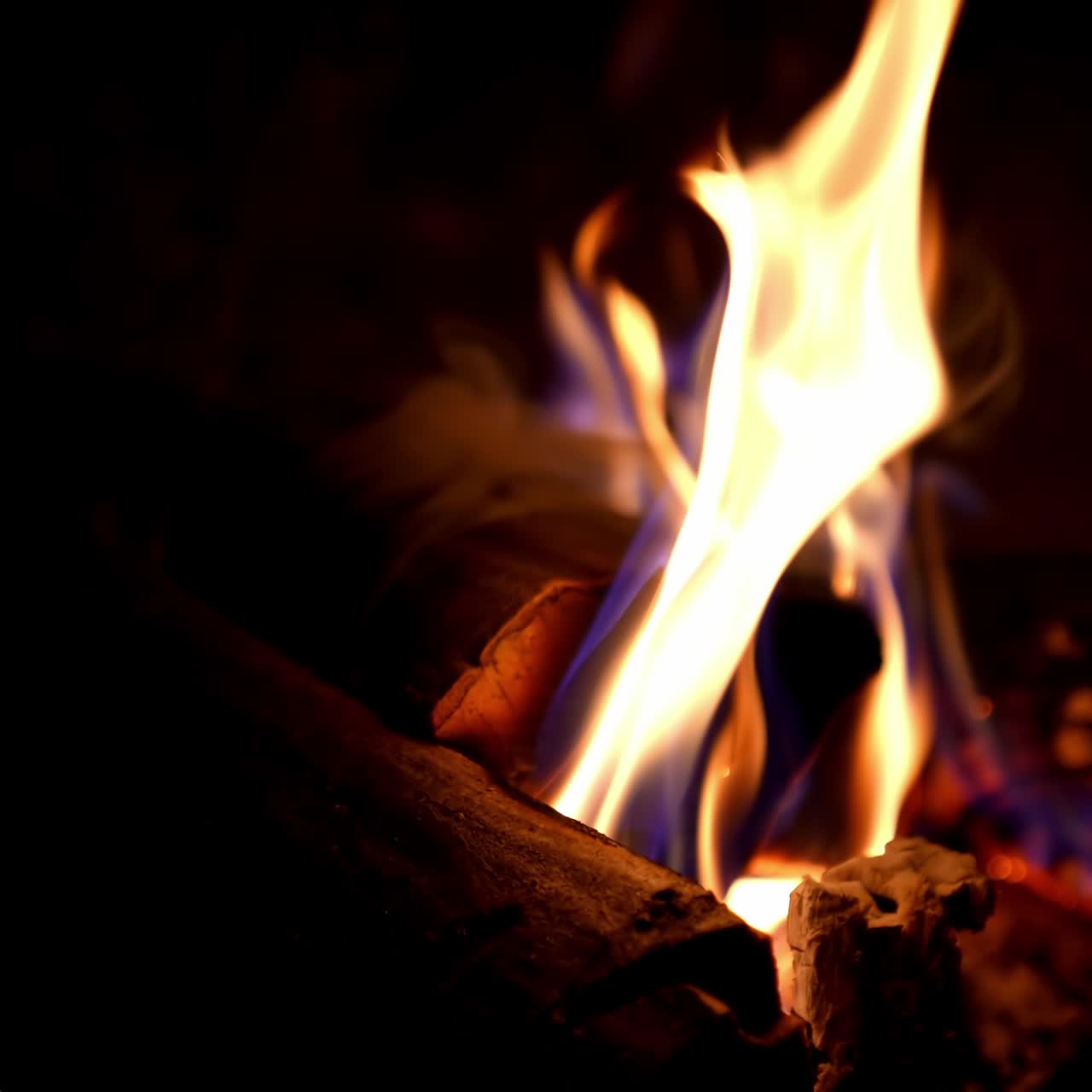 Fire in fireplace. Firewood burning in fireplace for heating at home in winter season. Wooden logs in flame on dark background. Macro shot