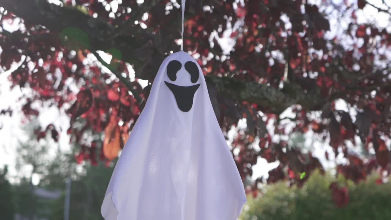 Close up tracking shot of scary Halloween ghost decoration hanging on a tree and swaying with the wind