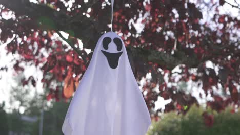 Close-up-tracking-shot-of-scary-Halloween-ghost-decoration-hanging-on-a-tree-and-swaying-with-the-wind