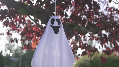 primer plano de seguimiento de la aterradora decoración fantasma de halloween colgando de un árbol y balanceándose con el viento