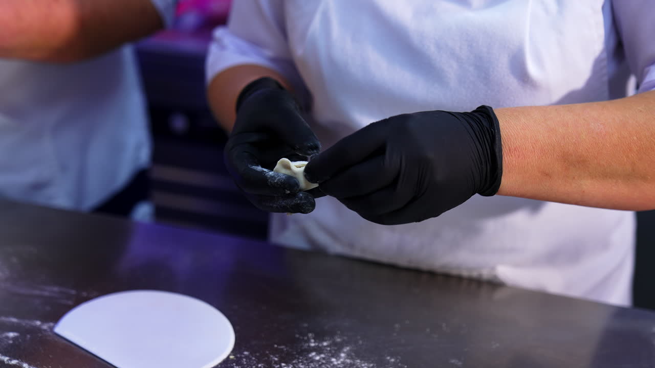 Gloved hands of a cook make the little dumplings. Two people making ravioli with meat at modern food factory.
