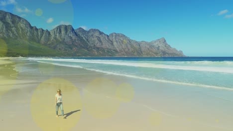 Multiple-light-spots-floating-against-caucasian-woman-walking-at-the-beach