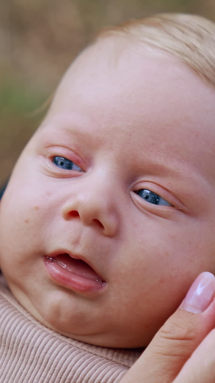 Blond baby boy with adorable blue eyes lies on mom's laps. Mother touches her kid's cheeks and nose. Close up. Vertical video