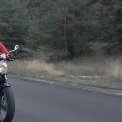 Motorcyclist-rides-along-forest-on-cloudy-day