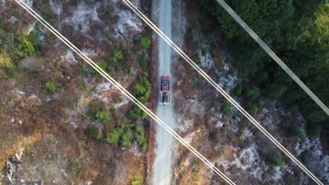 top view drone shot following a pickup truck on a gravel road driving into the forest below powerlines