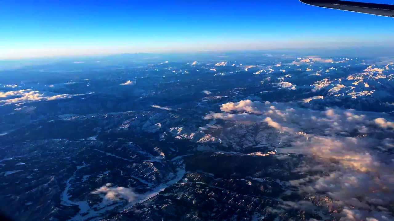 Flying on an airplane looking out the window, over mountains in the winter.