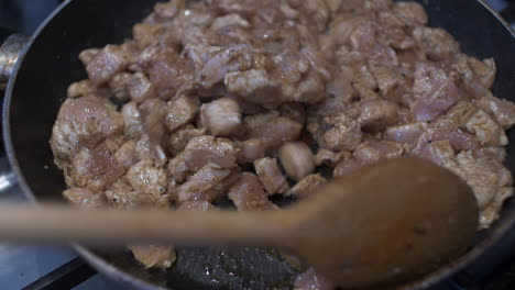 wooden spoon stirring diced chicken pieces in hot pan