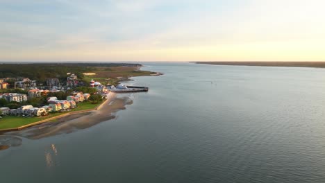 Glide over boats and lighthouse at harbor town pier as sun dips near horizon, panoramic aerial of Harbour Town Pier South Carolina USA