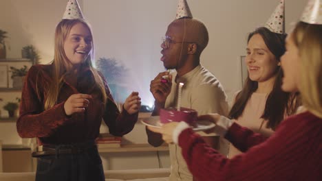 group of friends in birthday party, girl blows out a candle on the birthday cake making a wish