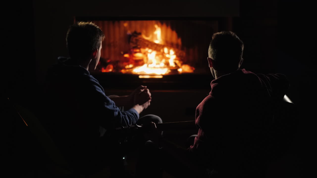 los amigos descansan en casa junto a la chimenea y un hombre toca la guitarra