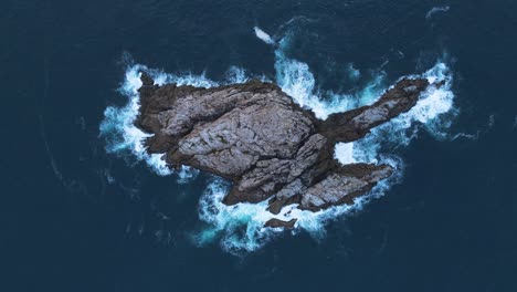 unique aerial view of waves crashing on fish rock cave surrounded by deep blue ocean waters