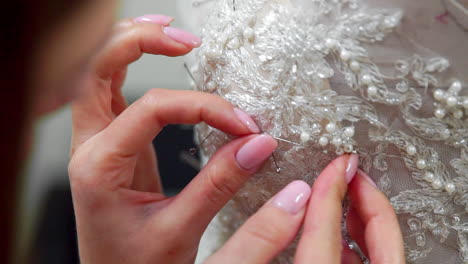 Close-up-fashion-designer-for-brides-in-his-Studio-pins-needles-lace-wedding-dress.-Seamstress-creates-an-exclusive-wedding-dress.-Secure-with-pins-and-needles-outline.-Small-private-business.-Sew-rhinestones-and-crystals-to-the-dress-thread-and-needle.-Jewelry-work.