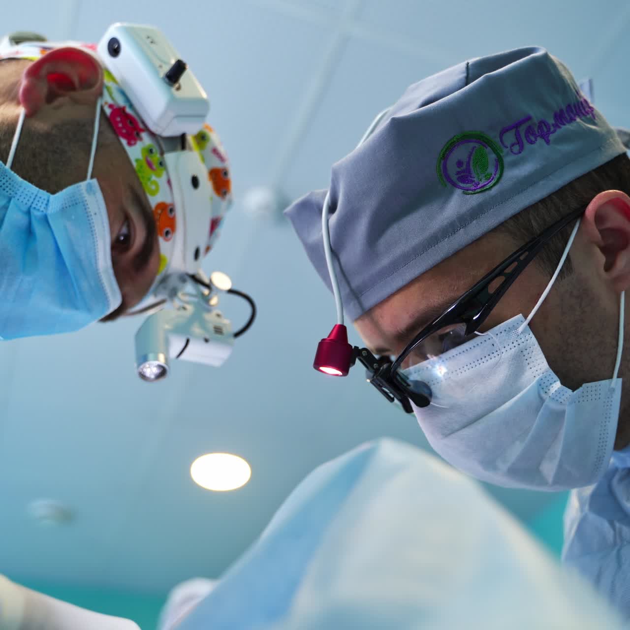 Two professional doctors wearing flashlights on their heads operating the patient. Low angle view on specialists at work. Close up