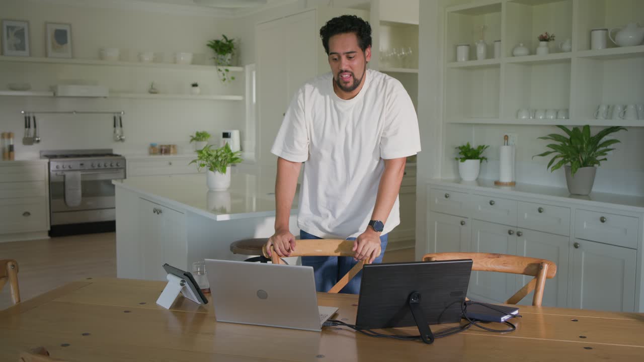 Uomo afroamericano che si avvicina a un tavolo di legno, stirando i polsi, digitando sul laptop per lavorare in cucina.