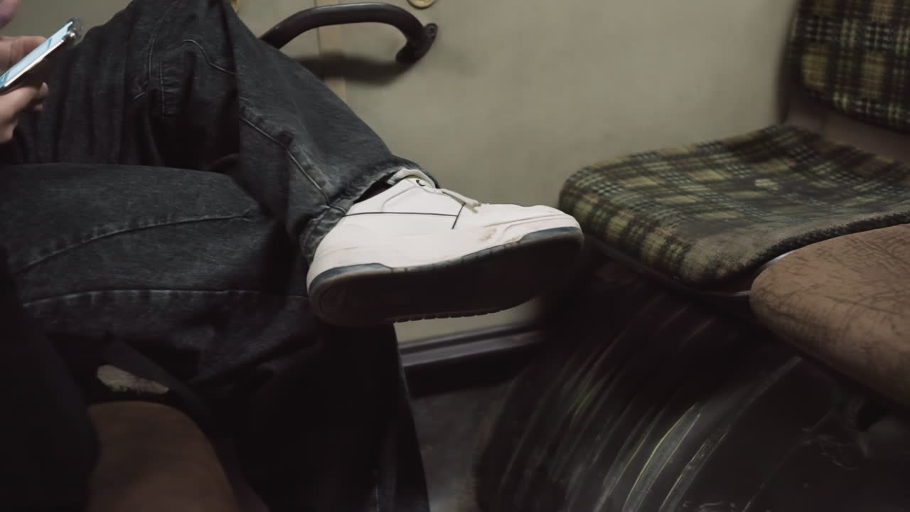 vista em close-up de uma pessoa sentada em um carro com as pernas cruzadas, segurando um smartphone, vestindo uma roupa casual, tênis brancos e o aconchegante
