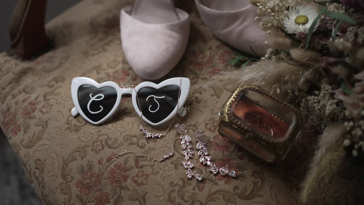 Close up of heart shaped sunglasses with initials beside wedding shoes and bridal jewelry