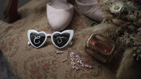 close up of heart shaped sunglasses with initials beside wedding shoes and bridal jewelry