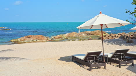 two empty sun loungers under a sun umbrella facing a picturesque sandy beach and ocean view